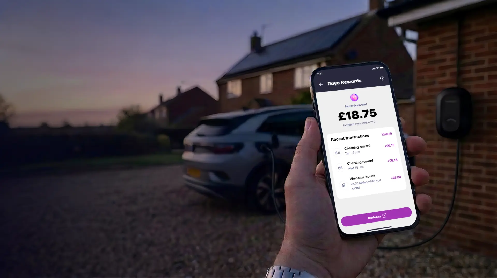A hand holding a phone showing the Raya Rewards balance on a driveway at dusk, with an electric car charging beside a home charge point